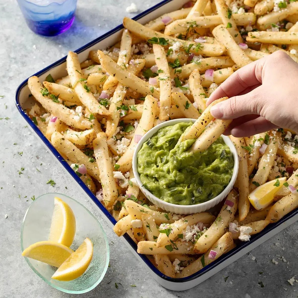 Crispy French fries with guacamole and lemon wedges for a delicious snack experience.